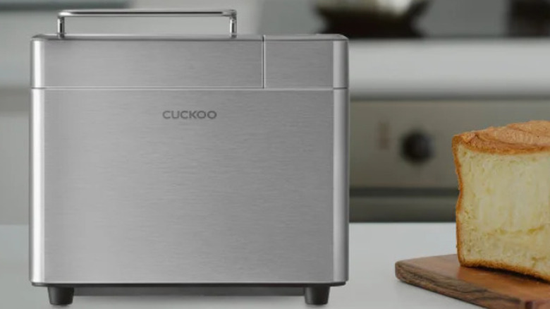 A Cuckoo bread maker on a counter next to loaf of bread