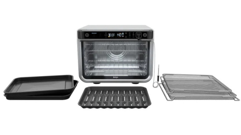 An empty Ninja Foodi air fryer on a white background surrounded by sheet pans and cooling racks