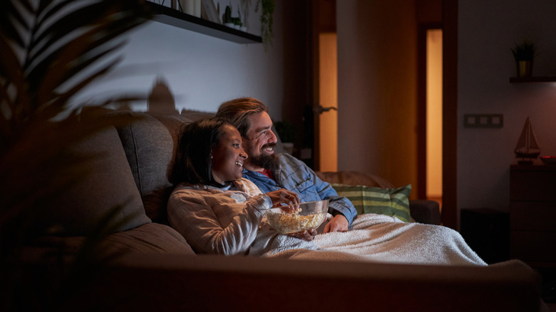 Two people on a couch watching a movie with a bowl of popcorn