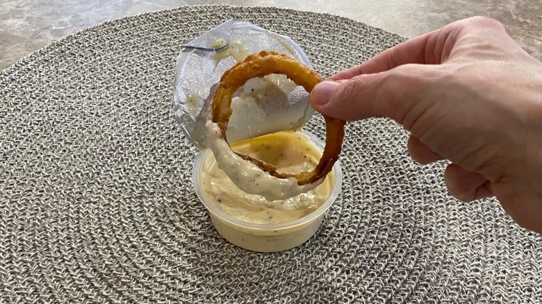 A hand dipping a Culver's onion ring into Signature sauce