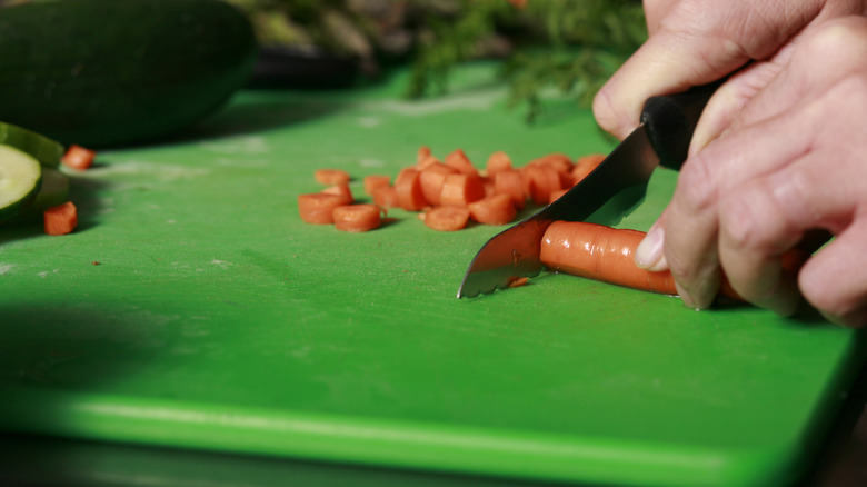 A person cutting carrots on green cutting board