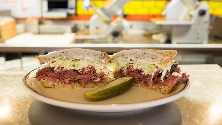 A pastrami sandwich with a pickle on a kitchen countertop