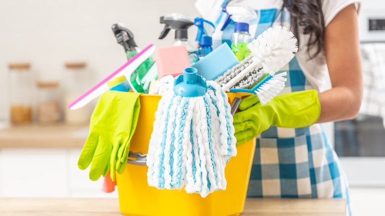 Woman holding Bucket full of a variety of cleaning products