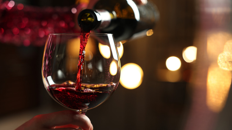 Someone pours red wine from a bottle into a wine glass