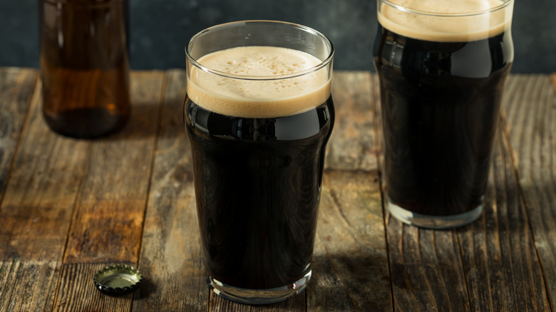 Two glasses of dark, stout beer sit atop a wooden table