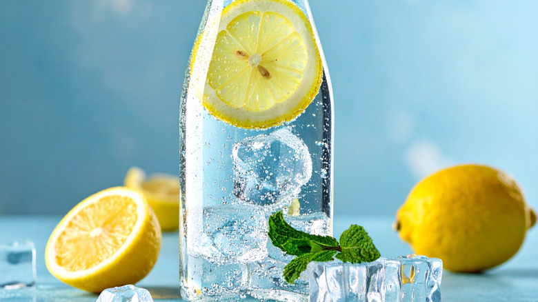 A bottle of sparkling water with ice and a lemon slice