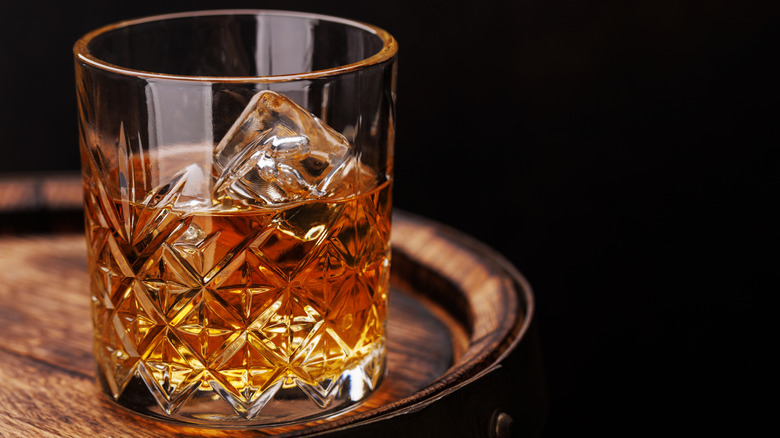 A glass of Scotch on the rocks sits atop a circular wooden table