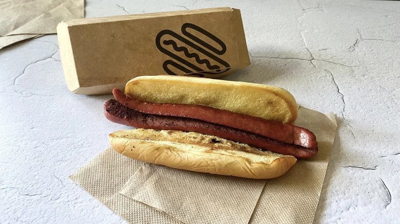 A Shake Shack hot dog on a napkin with the brand's box behind it.
