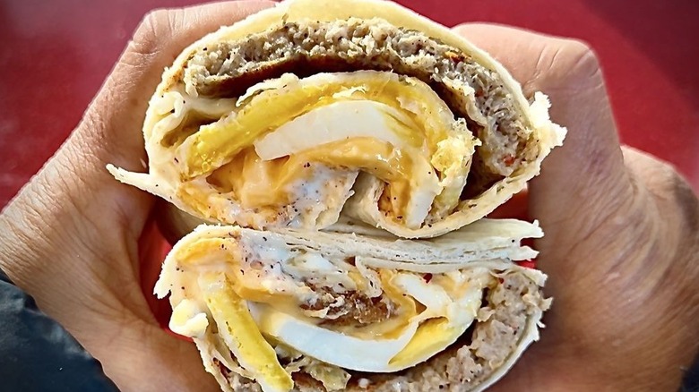 A person holding a Sausage Breakfast Burrito from Wendy's