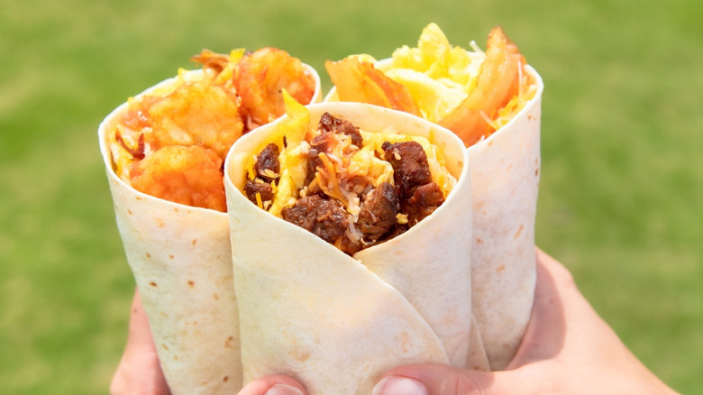 A person holding three breakfast burritos from Carl's Jr.