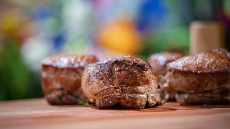 Three seared filet mignon steaks on a wooden board.
