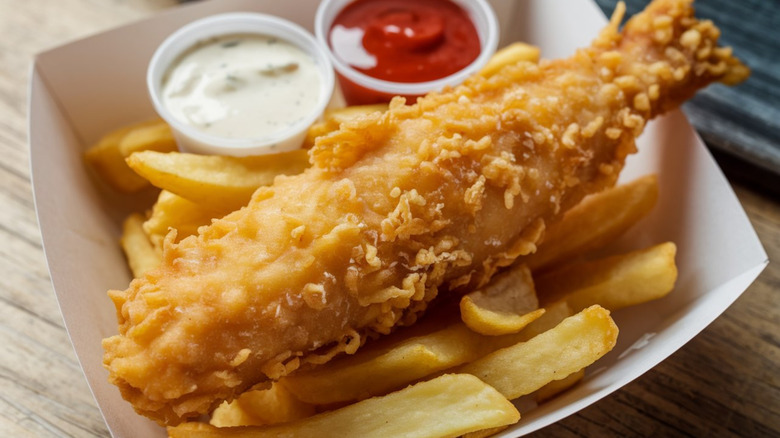 Fish and chips in a paper tray with tartar sauce and ketchup