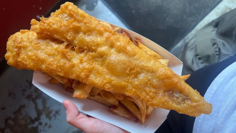 A person holding a paper tray of fish and chips at The Codfather