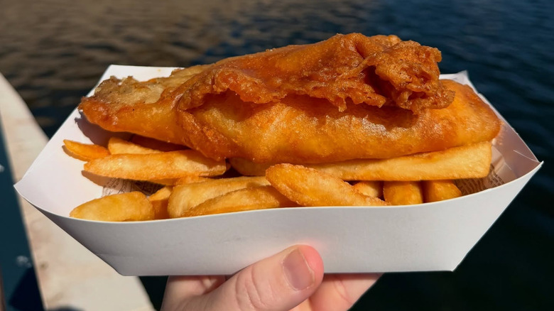 A person holding fish and chips in a paper carton from Yorkshire County Fish Shop