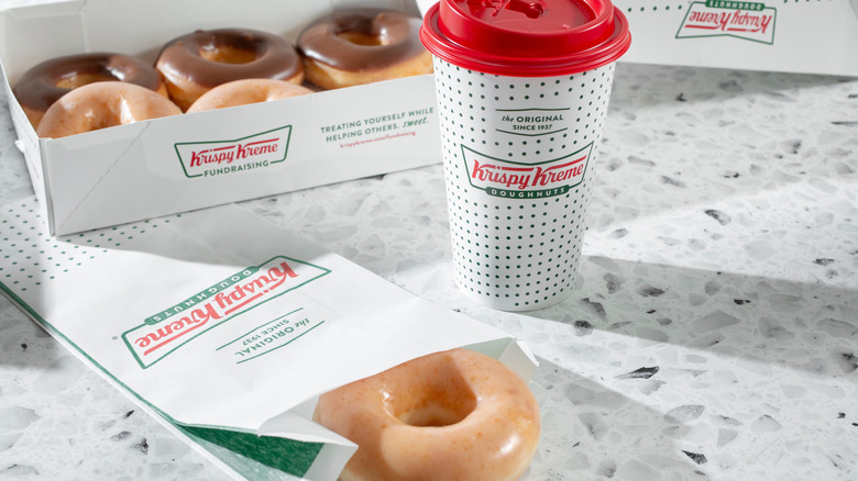 A box of Krispy Kreme doughnuts, plus one in a single sleeve and a cup of coffee.
