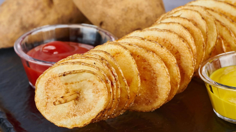 Potato crisps twirled around a wooden skewer with side dishes of ketchup and mustard