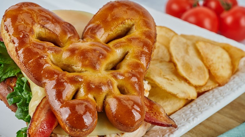 A club sandwich inside a butterfly-shaped pretzel bun with potato chips on the side