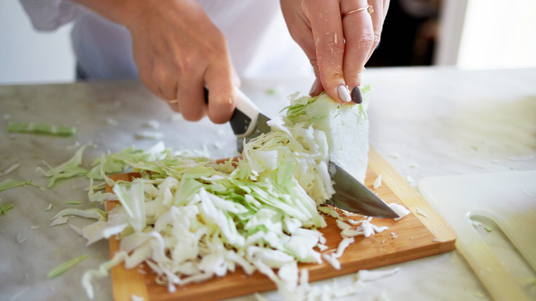 person standing and chopping green cabbage on chopping board