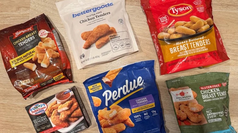 Six different brands of frozen and bagged chicken tenders lay on a wooden table