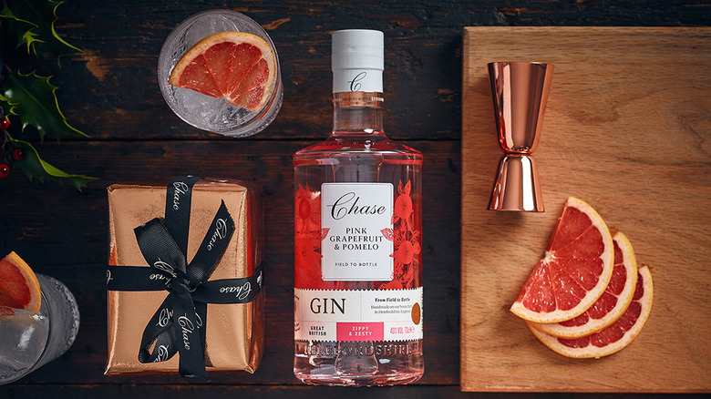 Bottle of Chase Distillery Pink Grapefruit & Pomelo Gin with cocktails, fresh sliced grapefruit, and a jigger