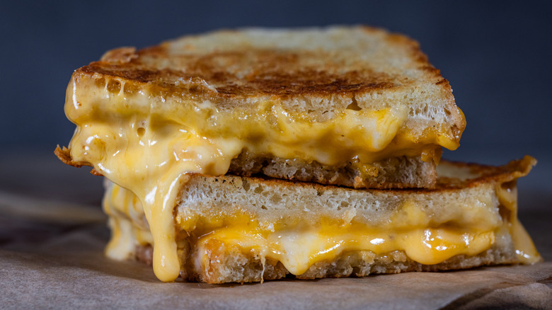 Grilled Cheese with melting cheese dripping from the inside. The sandwich is cut in half and placed on a wooden cutting board.