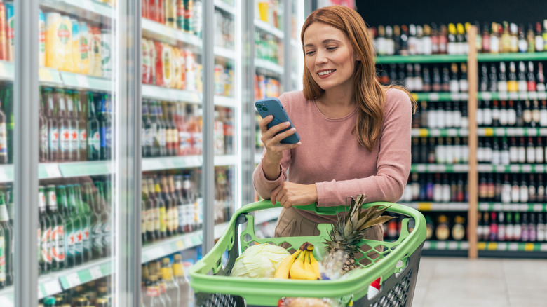 Woman holding phone while standing in grocery store aisle