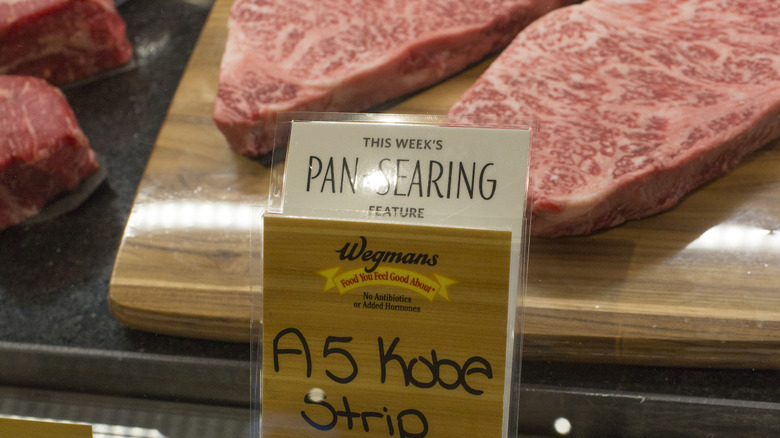 Two A5 Wagyu strip steaks in a butcher case at Wegmans with a Wegmans label in front