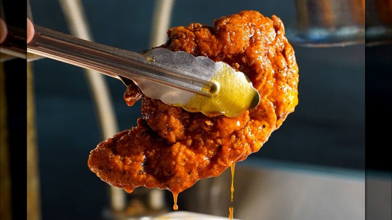 Tongs holding dripping hot chicken