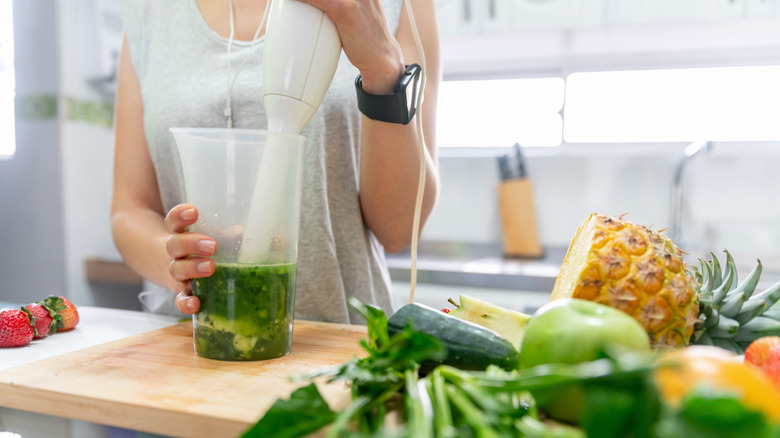 woman using immersion blender to blend up a green smoothie