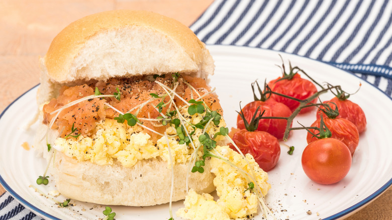 Smoked salmon and egg salad sandwich on a plate with roasted tomatoes on the vine