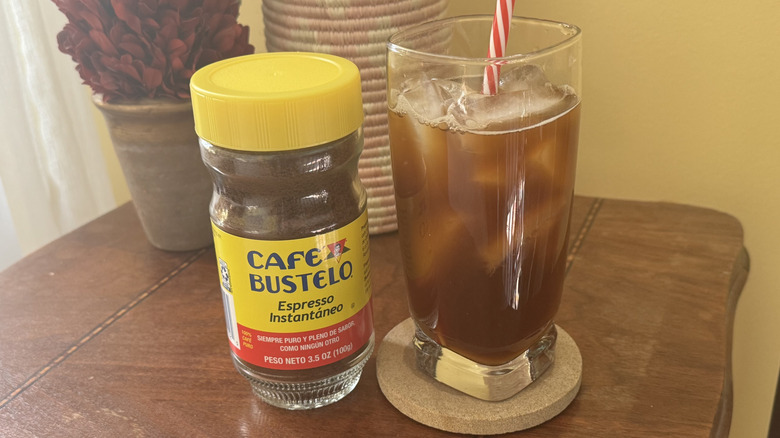 A glass of iced coffee sitting on a table next to a Cafe Bustelo cannister