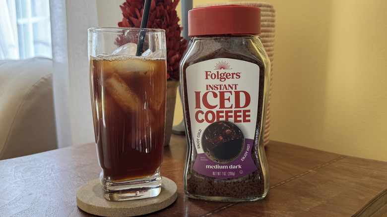 A glass of iced coffee on a table next to a cannister of Folgers Instant Iced Coffee