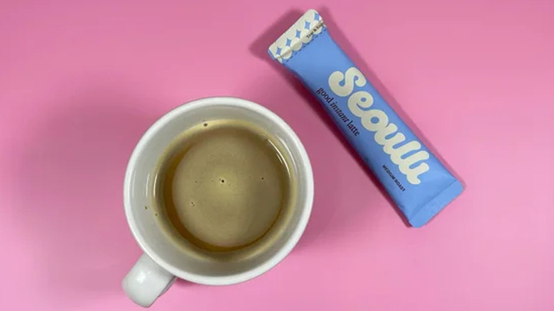 A cup of coffee next to a sachet of Seoulli instant latte mix