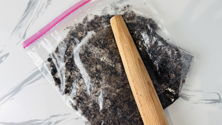 bag of chocolate cookie crumbs with a rolling pin on top