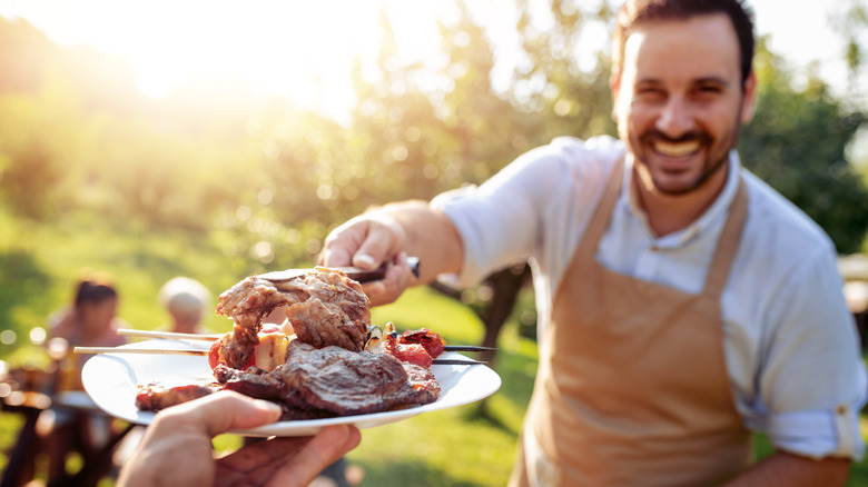 Person grilling and putting meat on a plate.