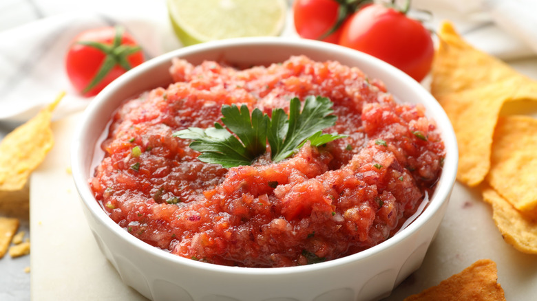 Bowl of salsa with tomatoes and tortilla chips in the background