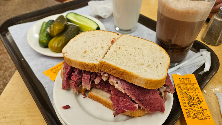 A pastrami sandwich  on a tray with pickles and drinks at Katz's Delicatessen in New York City