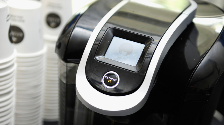 A Keurig machine with paper cups stacked in the background