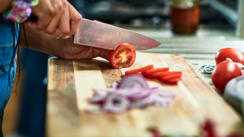 Someone slicing a tomato with a knife on a cutting board