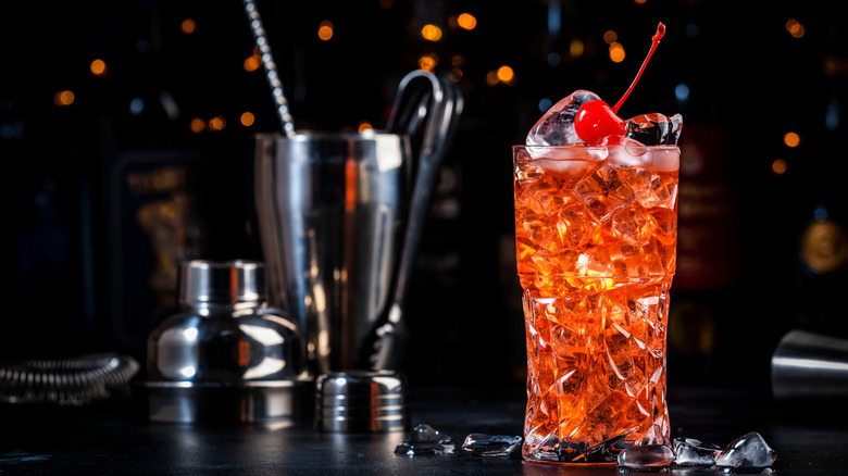 Cherry and amaretto cocktail on ice with mixologist tools in the background