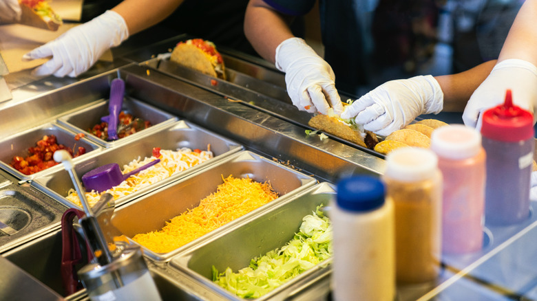 Team of Workers Preparing Mexican Tacos with Fresh Ingredients at Fast Food Restaurant Counter