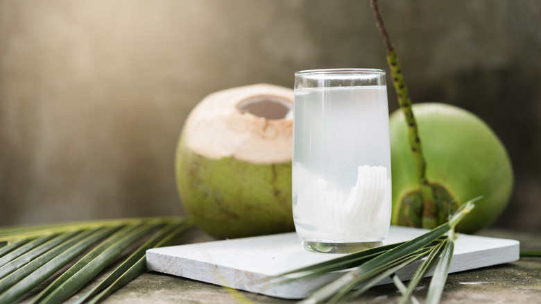 Coconut water on marble slab in front of coconuts.