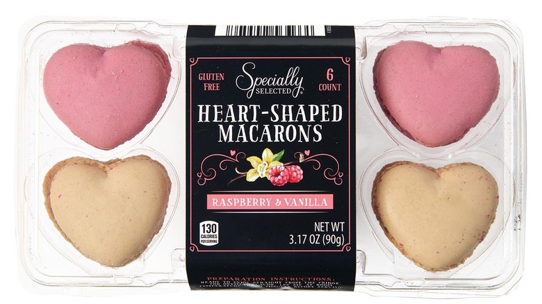 A clear package with heart-shaped macarons inside, showing two pink (raspberry) and two beige (vanilla).