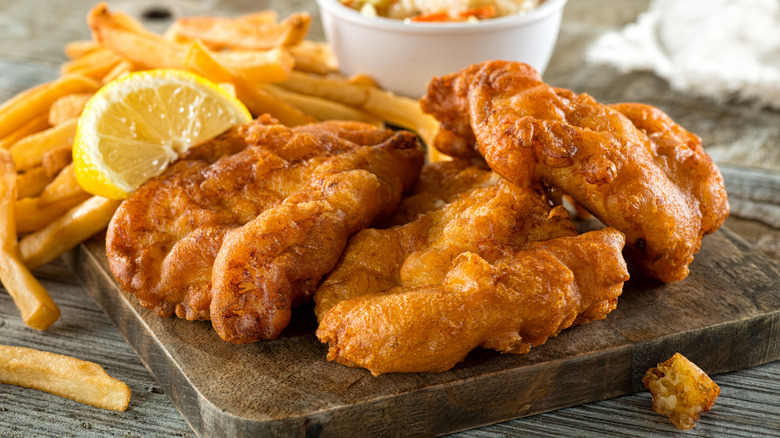 Fired fish pieces on a wooden board with fries and lemon wedge