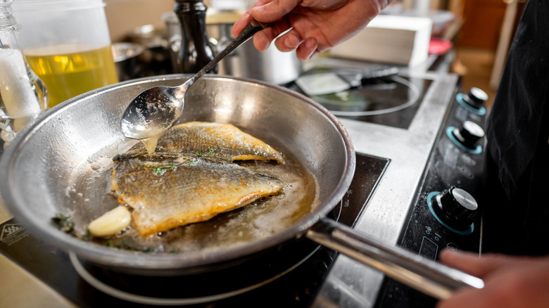 A chef frying fish in a stainless steel pan.