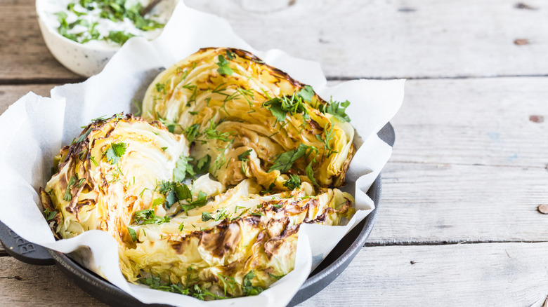 Tender baked cabbage served on white baking paper in ceramic dish on wood table.