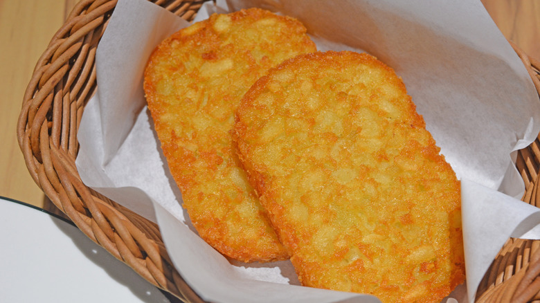 Two crispy, golden hash brown patties in a parchment paper-lined basket