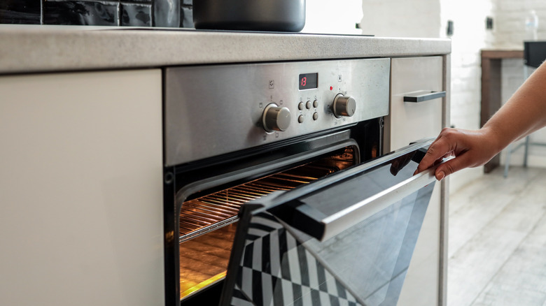 A person's hand is seen opening an oven door.