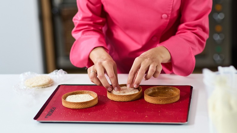 A female baker arranging tartlets on a red silicone baking sheet insert.