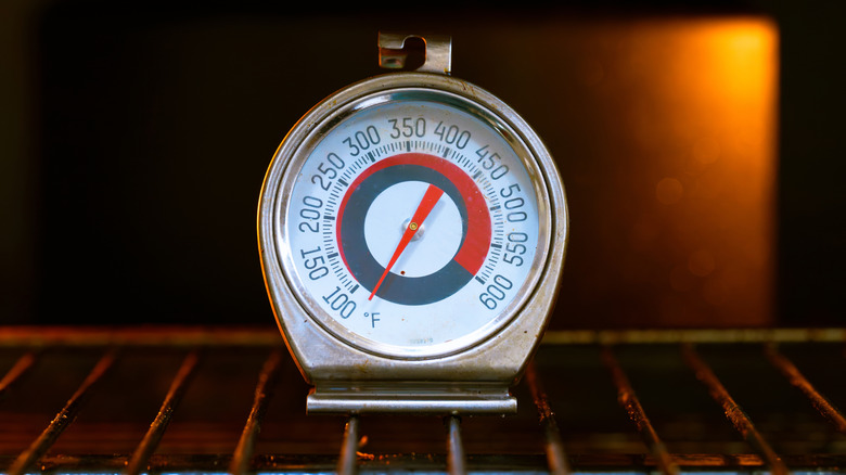 An analog oven thermometer sitting on an oven rack